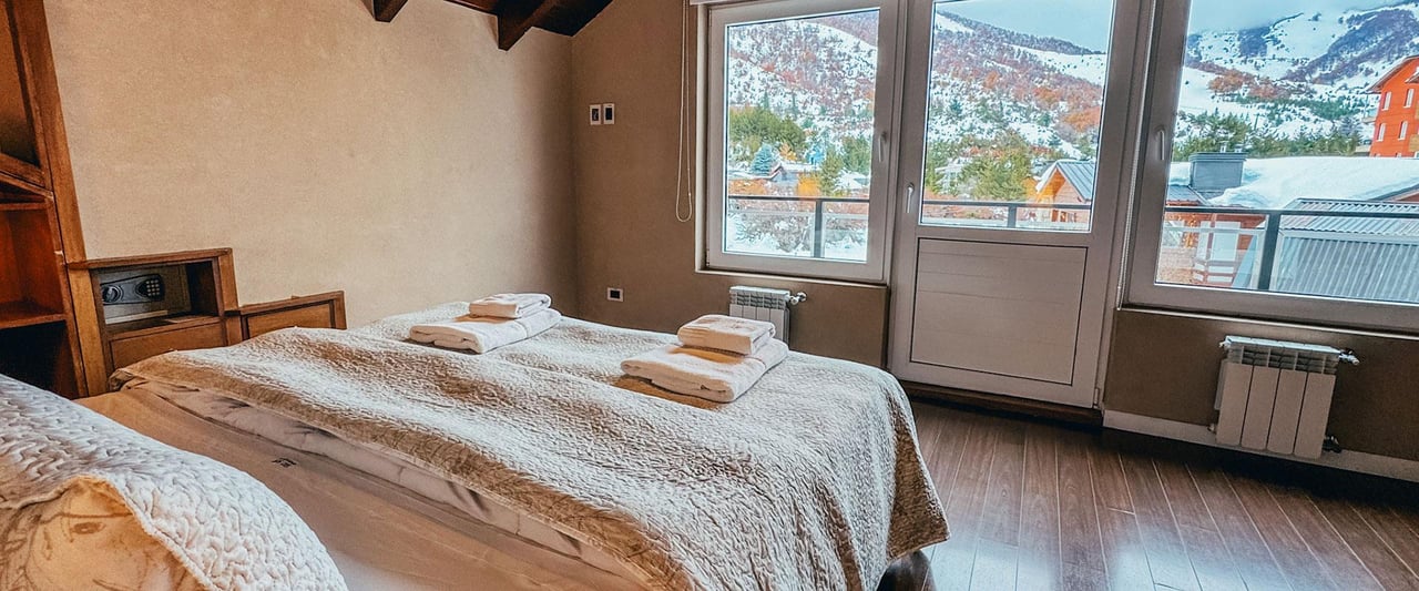 Furnished bedroom with a large bed and wide windows overlooking snowy mountains.