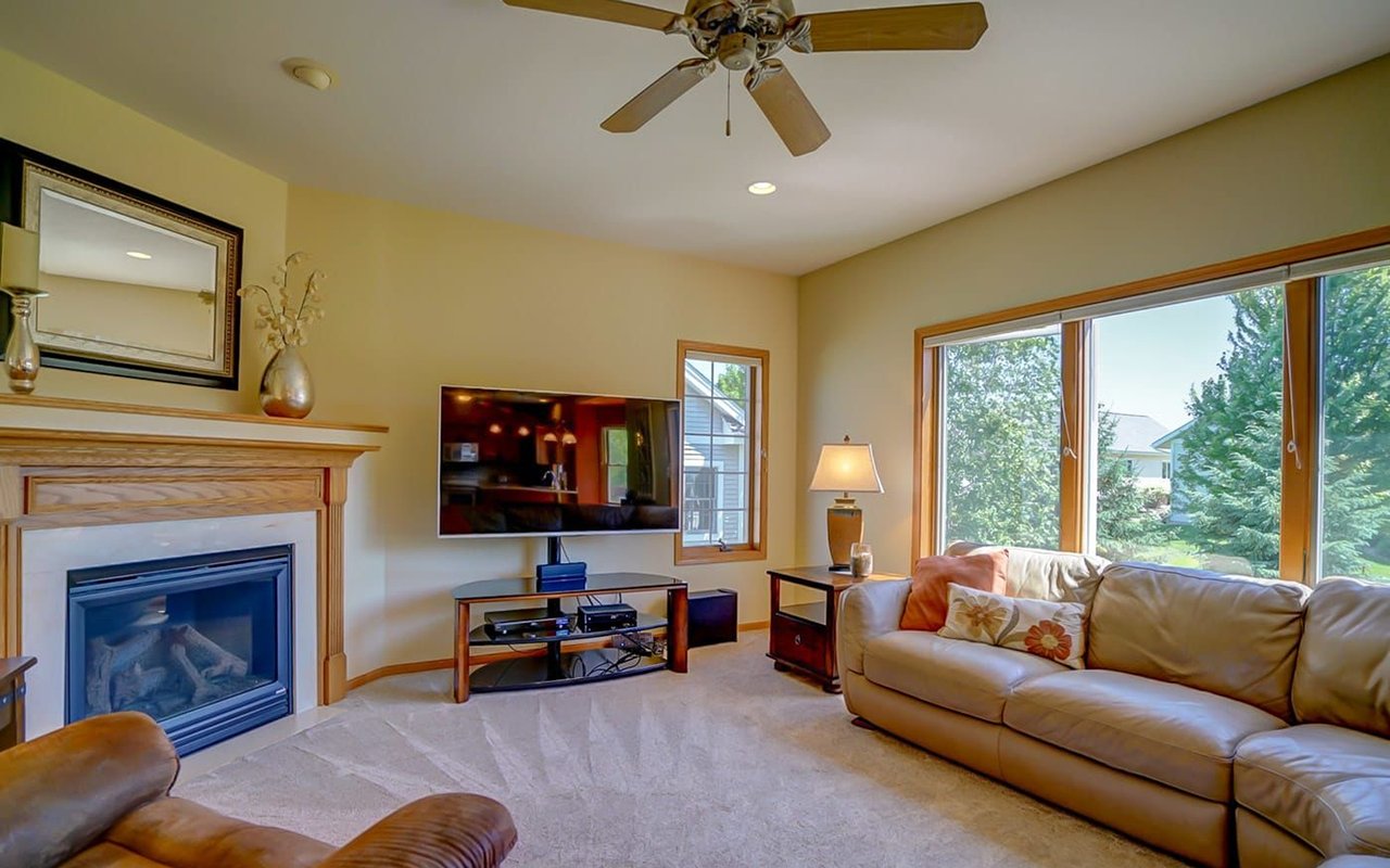 Living room with a fireplace, leather sofas, and large windows overlooking a green yard.