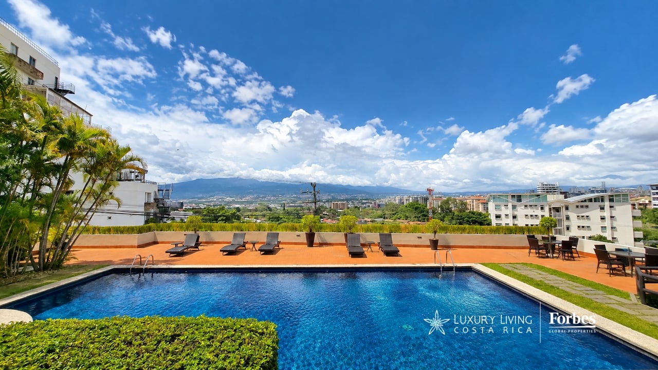 Condominium pool terrace with lounge chairs and views of the city and mountains.