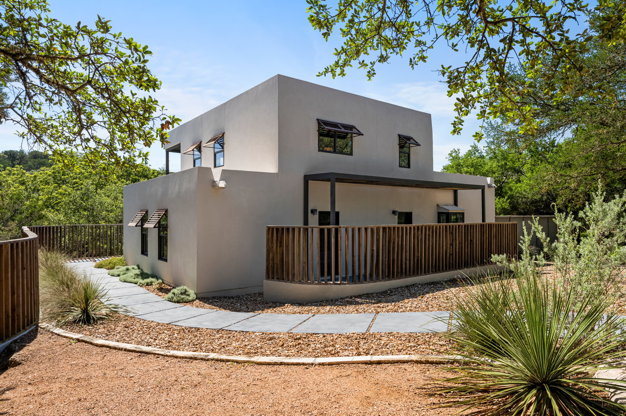 Modern two-story stucco home with a raised wooden deck and curved walkway through drought-tolerant landscaping.