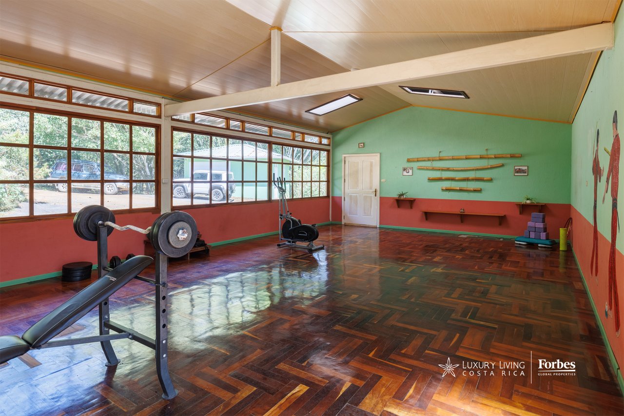 Home gym with weight bench and stationary bike beside expansive windows and parquet flooring.