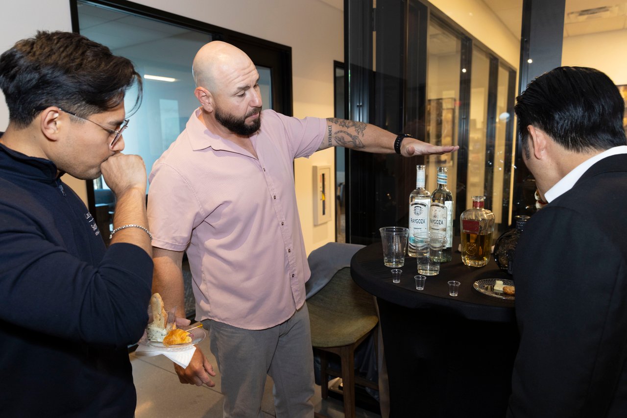 Men chat around a refreshments table at an indoor open house.