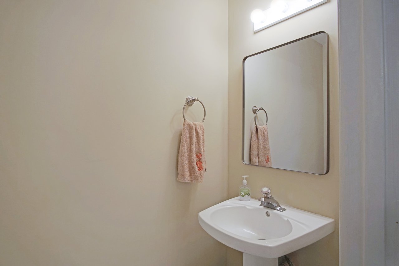 Half bathroom at 529 Collinsford Road, Tallahassee, Florida, featuring a pedestal sink with chrome faucet, wall-mounted mirror, and towel ring. The space has beige walls and overhead vanity lighting for a clean, simple design.