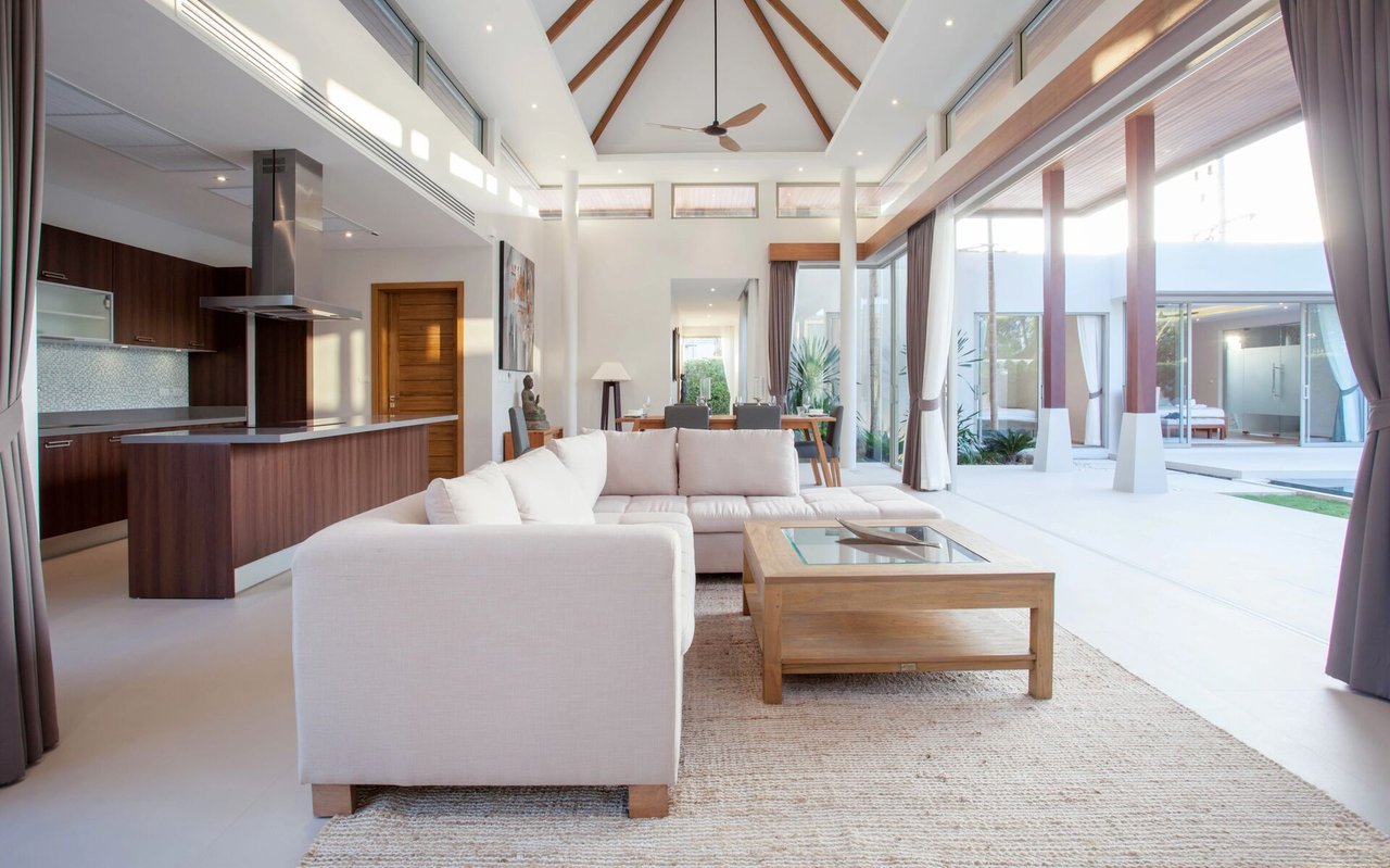 Modern living room with a white sectional, open kitchen, vaulted wood-beamed ceiling, and expansive glass doors.