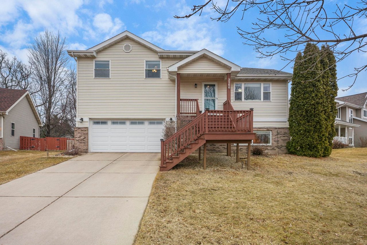 Exterior view of a classic bi-level single-family home with light siding, a two-car garage, and a wooden front staircase, representing the style of starter homes typically available under $450,000 in established Sun Prairie, WI neighborhoods.