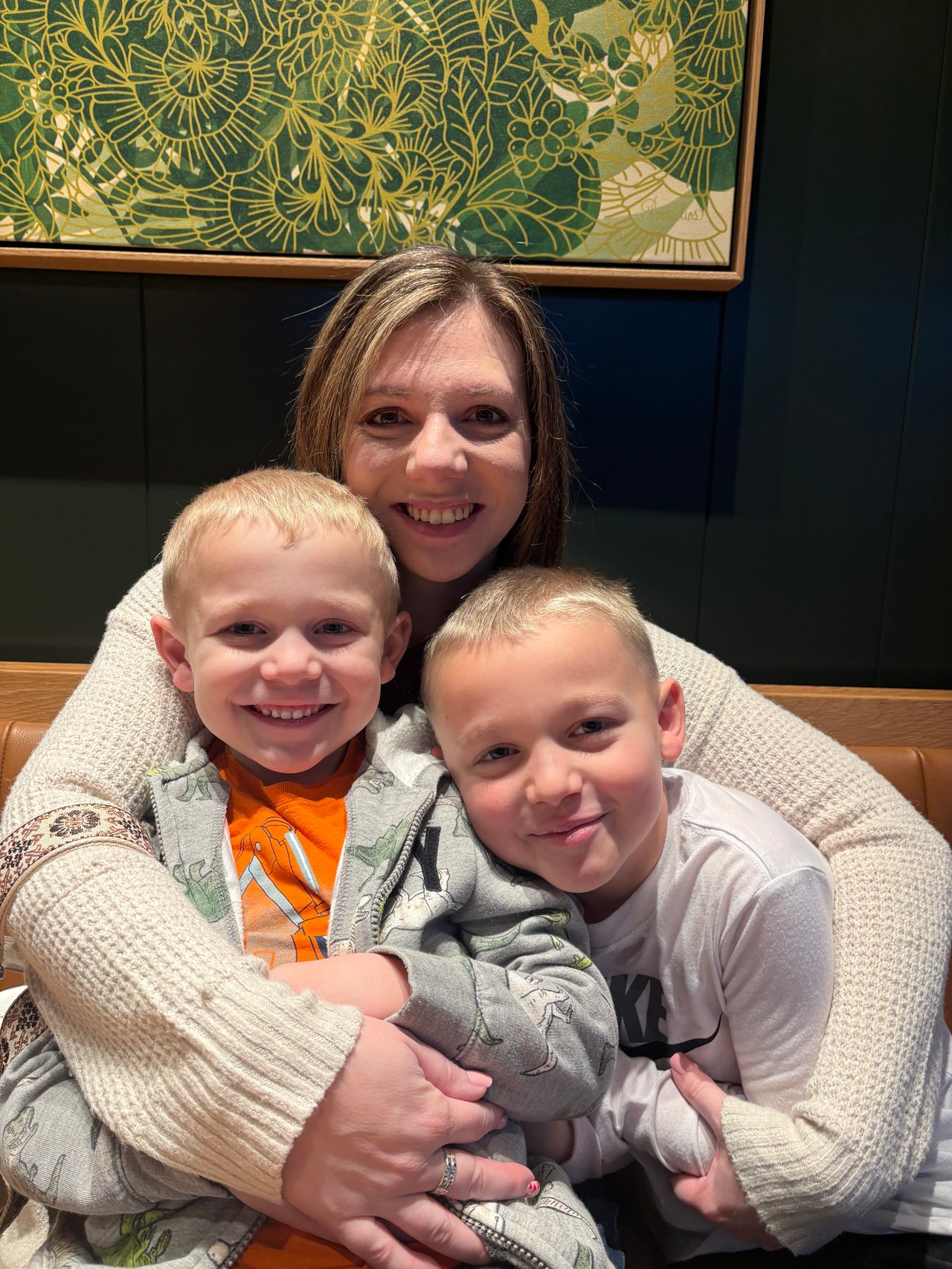 A woman smiling with two young boys in front of framed floral artwork.