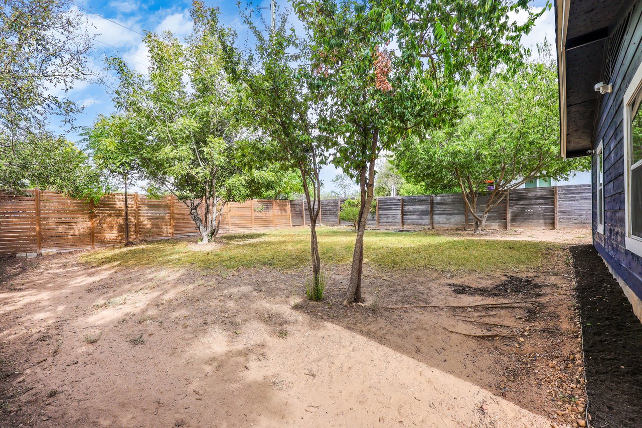 Backyard with mature trees, a mostly bare yard, and wooden privacy fencing.