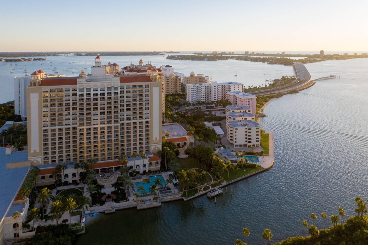Waterfront condominium towers beside Sarasota Bay, with pools and a curving bridge in the distance.
