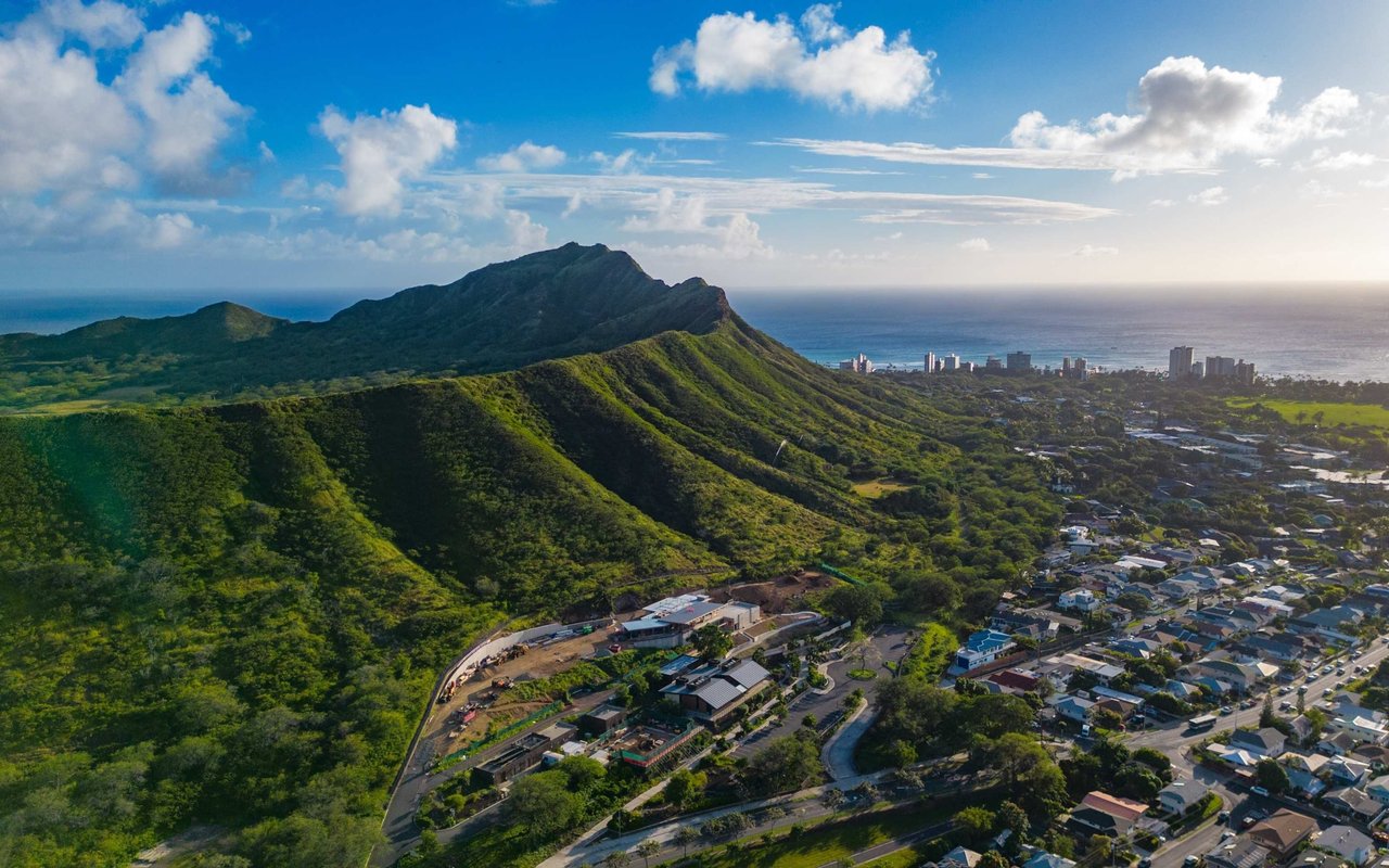 Aerial view of Diamond Head’s green ridge, Honolulu homes, and the Pacific Ocean.