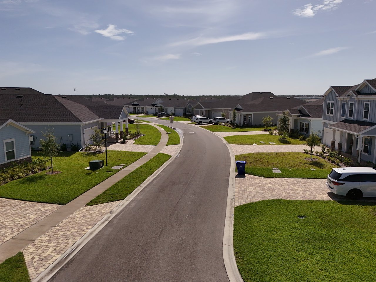 Residential street curving between homes with green lawns, sidewalks, and paved driveways.