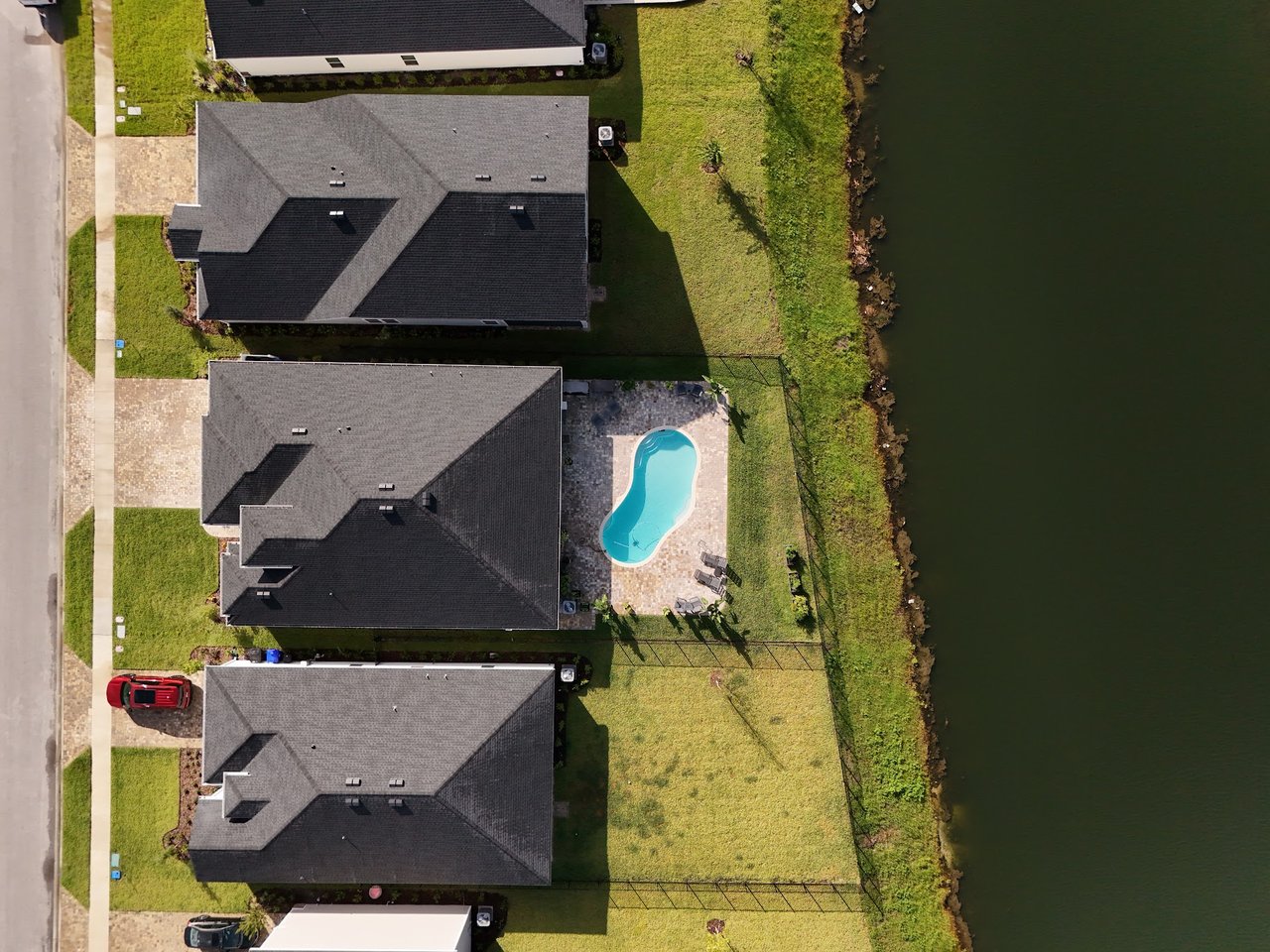 Aerial view of a home with a backyard pool beside a pond and neighboring houses.