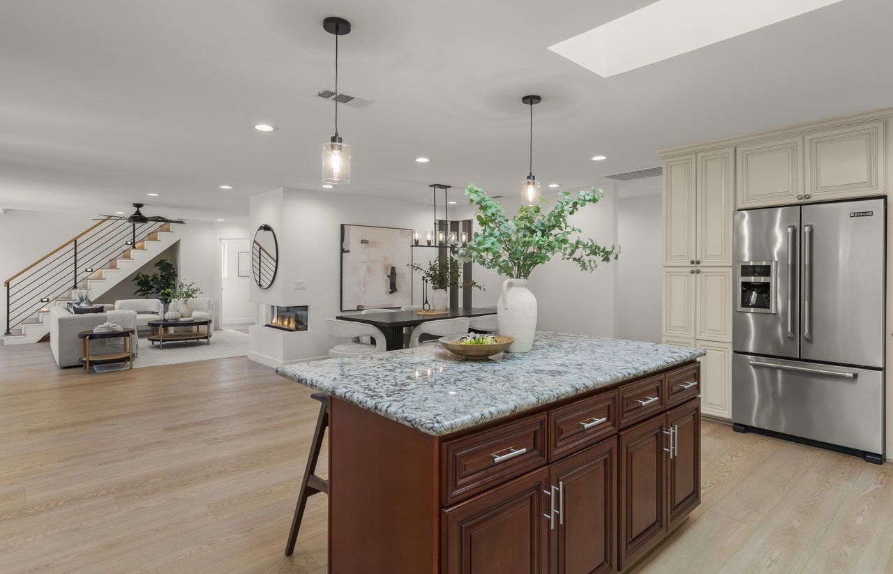 Open-plan kitchen with a large stone-topped island, cream cabinets, and a stainless steel refrigerator.