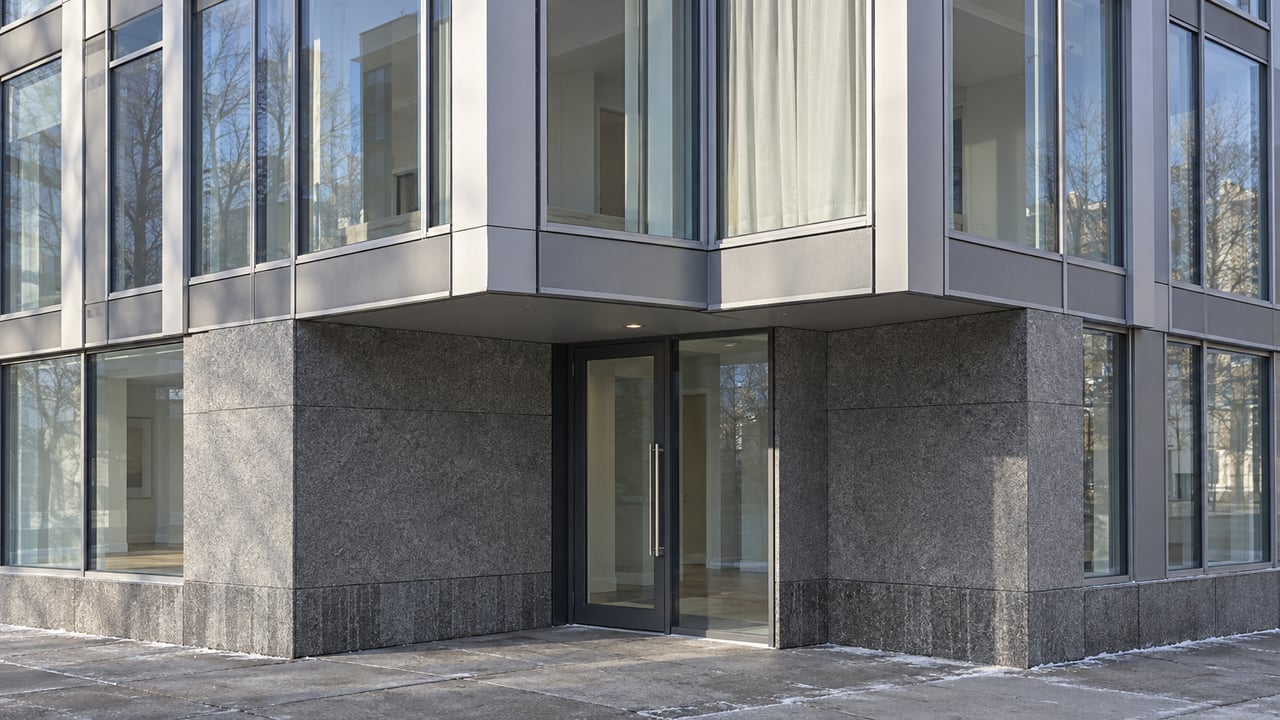 Winter sunlight on a contemporary apartment facade with aluminum-framed windows, a granite entrance recess, and a clear sidewalk.