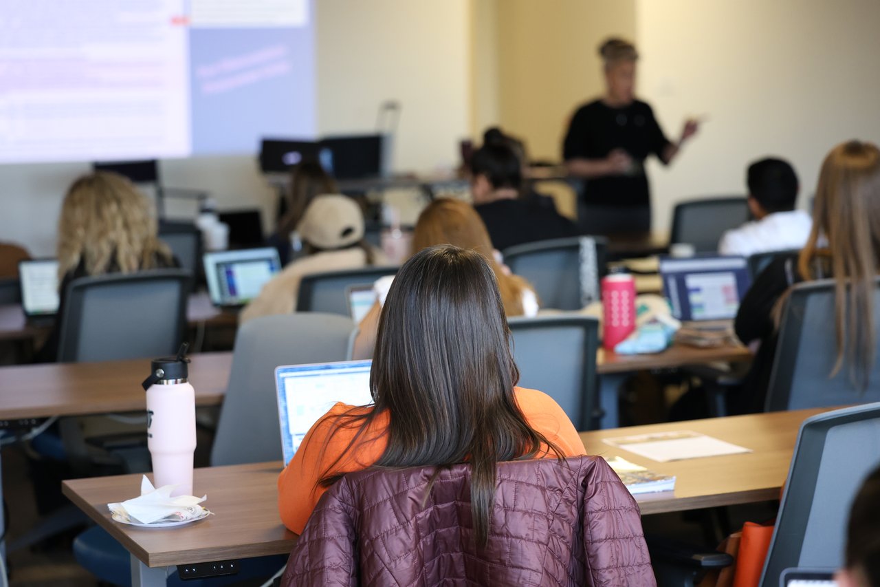 Real estate instructor presents to attendees seated with laptops in a classroom.