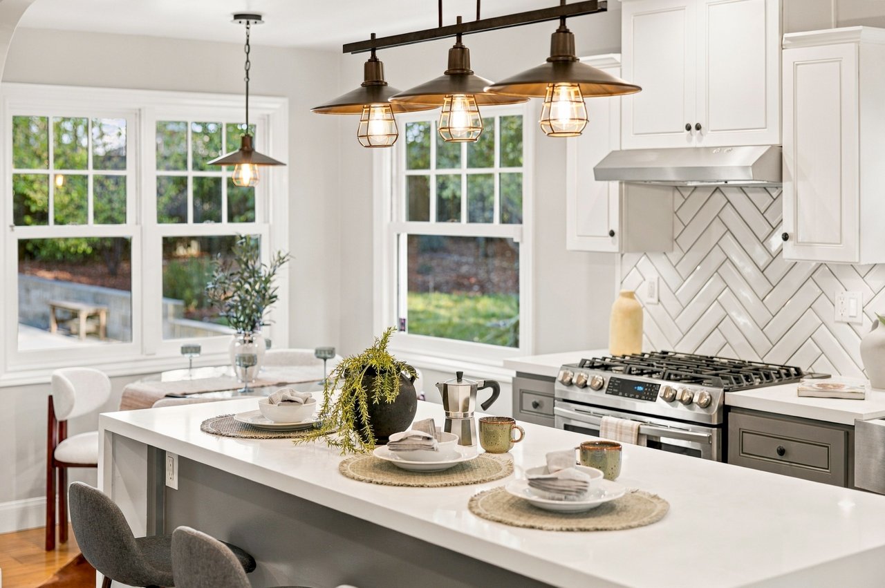 Bright kitchen with a large dining island, herringbone backsplash, and bronze pendant lights.