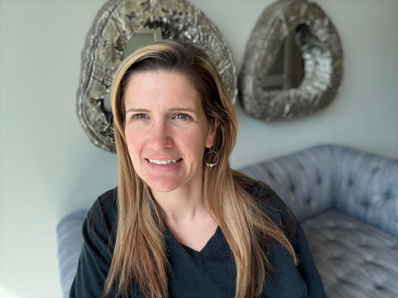 Amanda Hyde seated on a gray sofa with decorative mirrors behind her.