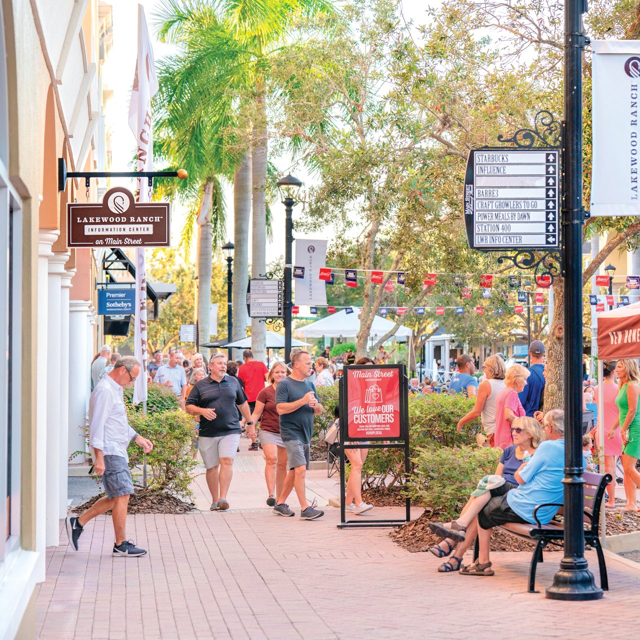 Lakewood Ranch Main Street with palm trees, shop signs, and a crowd of pedestrians.