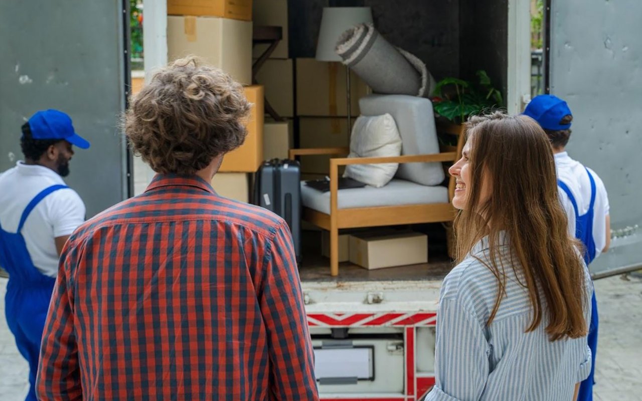 A couple watches two movers load furniture and boxes into a moving truck.