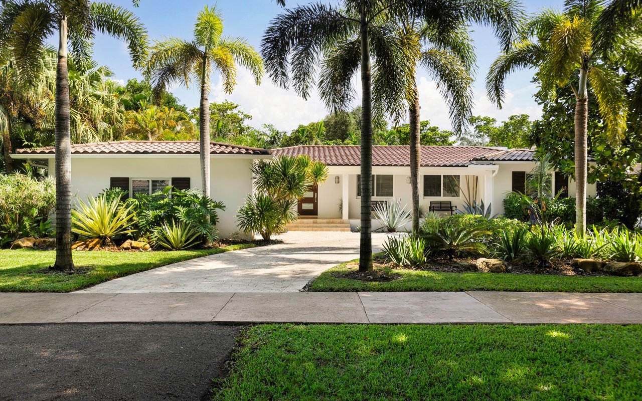 Single-story white house with a terracotta tile roof, palm trees, and tropical landscaping.