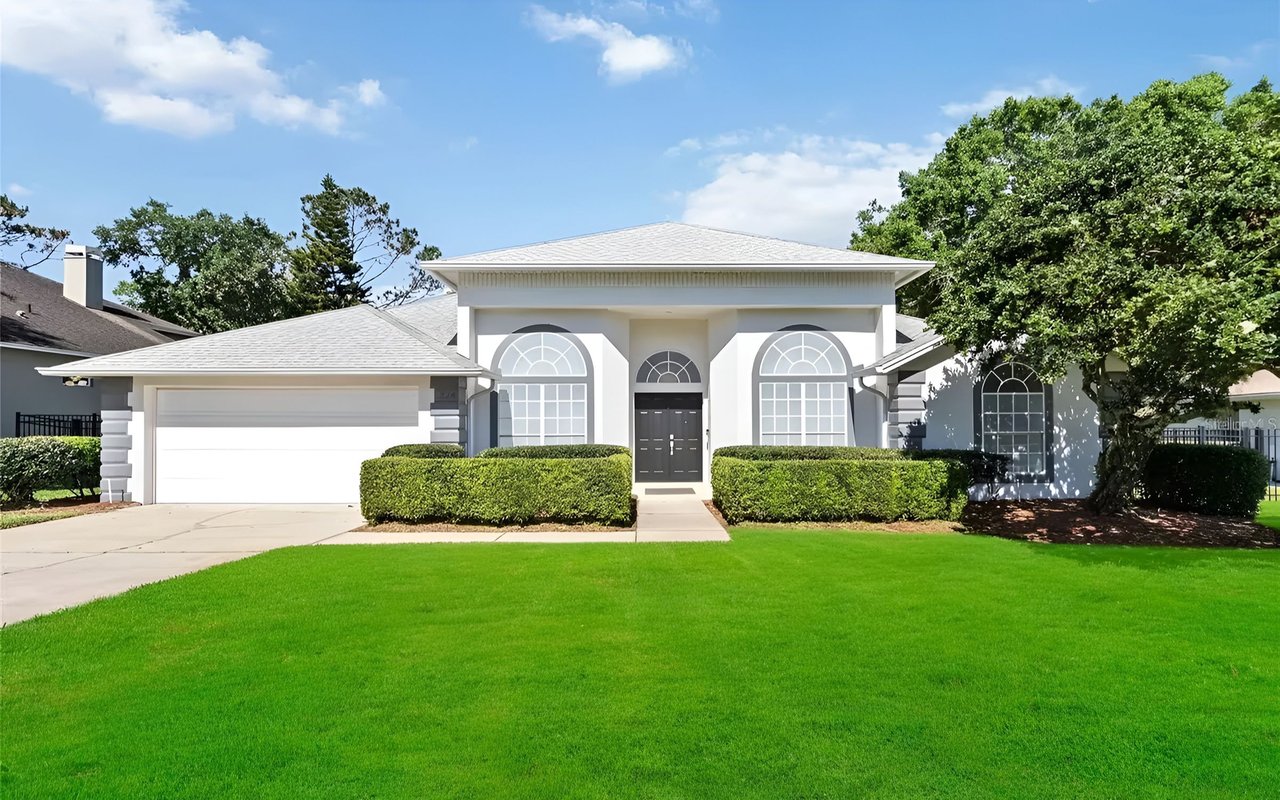 White home with arched windows, an attached garage, and a broad green lawn.