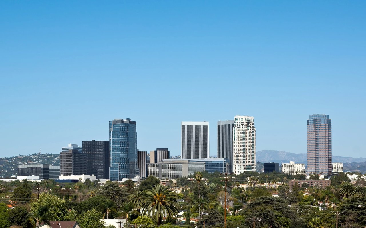 Los Angeles-area skyline rising above leafy homes and palm trees.