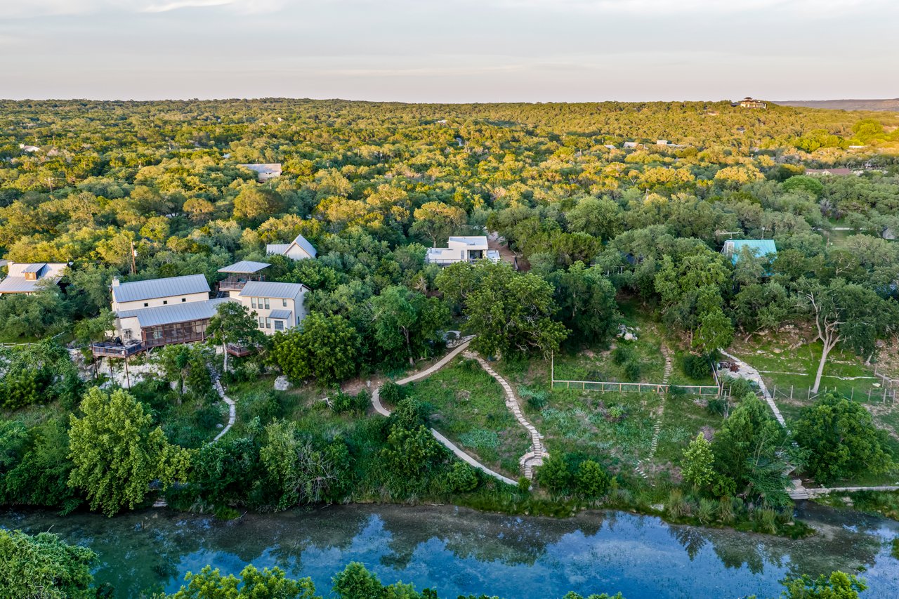 Aerial view of homes and winding paths among trees beside a clear river.