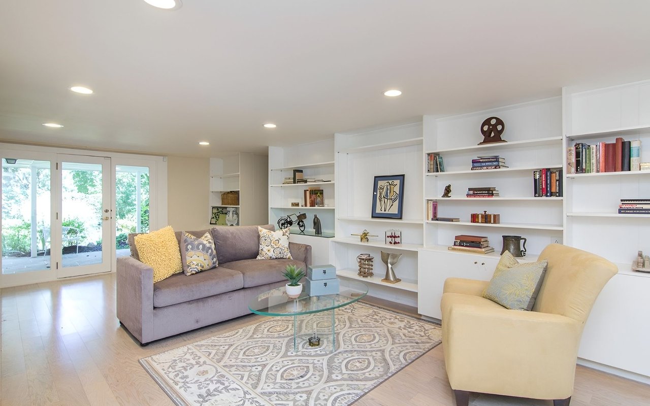 Living room with built-in white shelving, a gray sofa, and French doors to a garden.