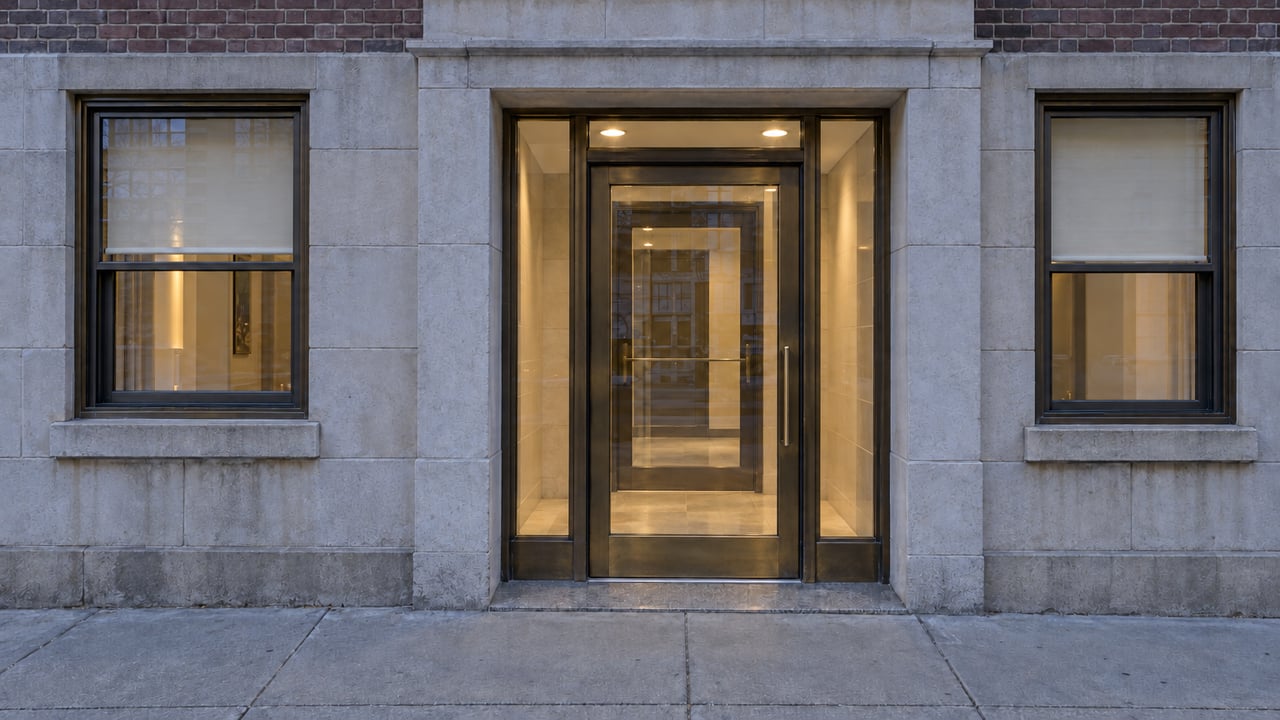 Unoccupied limestone apartment entrance with bronze-framed glazing and a warmly illuminated vestibule.