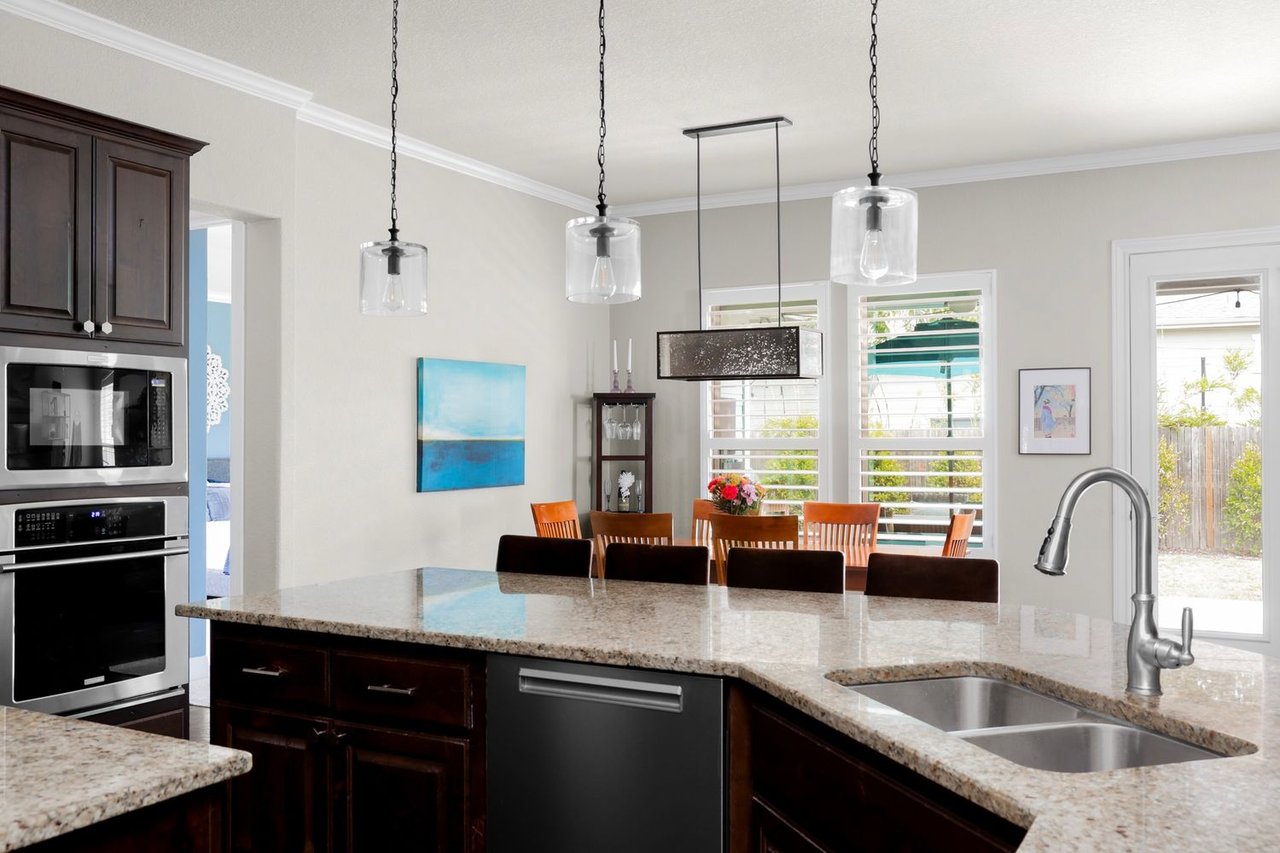 Kitchen with a granite island and double-basin sink, dark cabinetry, and a dining area by shuttered windows.