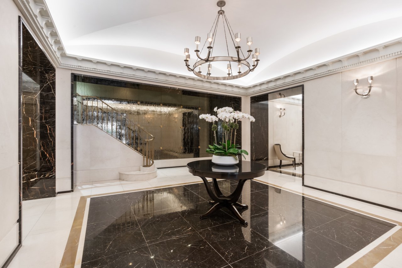 Building lobby with a curved staircase, marble floors, orchid centerpiece, and chandelier.