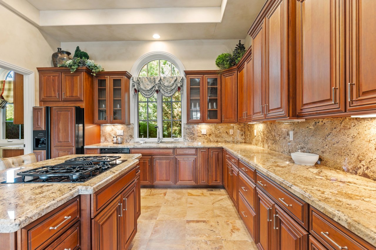 Guest-house kitchen with cherry wood cabinetry, granite counters, a gas cooktop island, and an arched window.