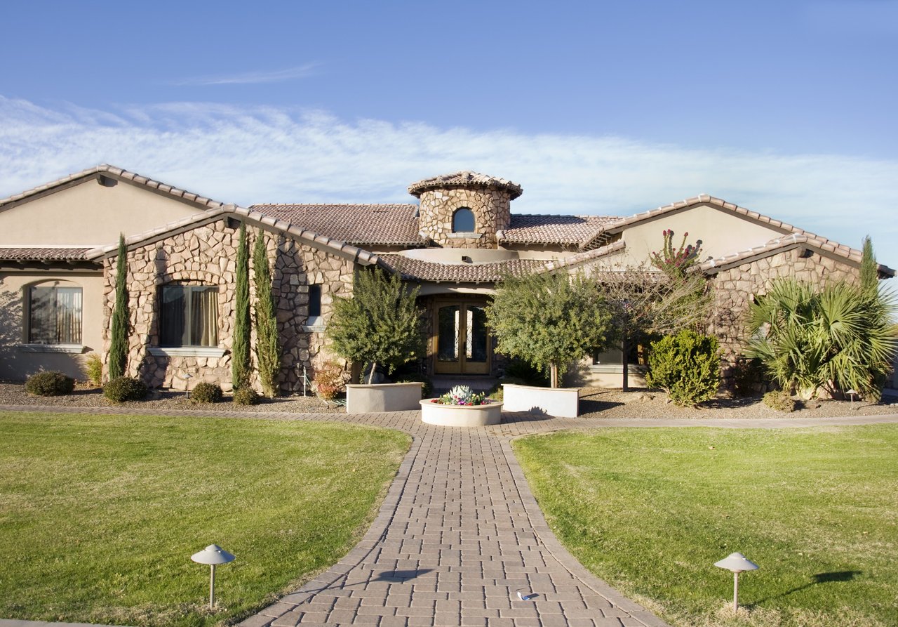 Stone-fronted home with a tiled roof, landscaped lawn, and brick walkway leading to the entrance.