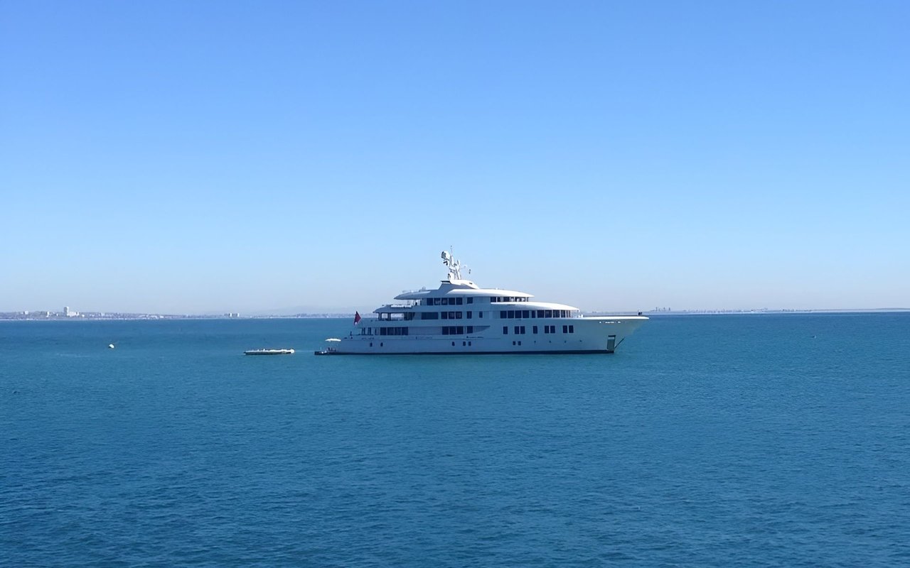 Large white yacht on blue water with a distant coastline.