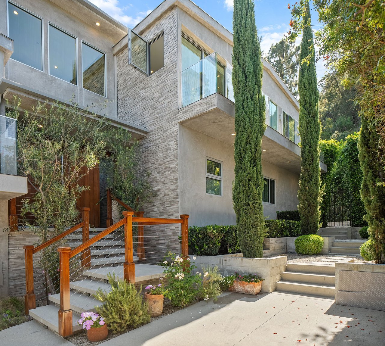 Modern home exterior with a glass balcony, stone facade, and landscaped entrance steps.