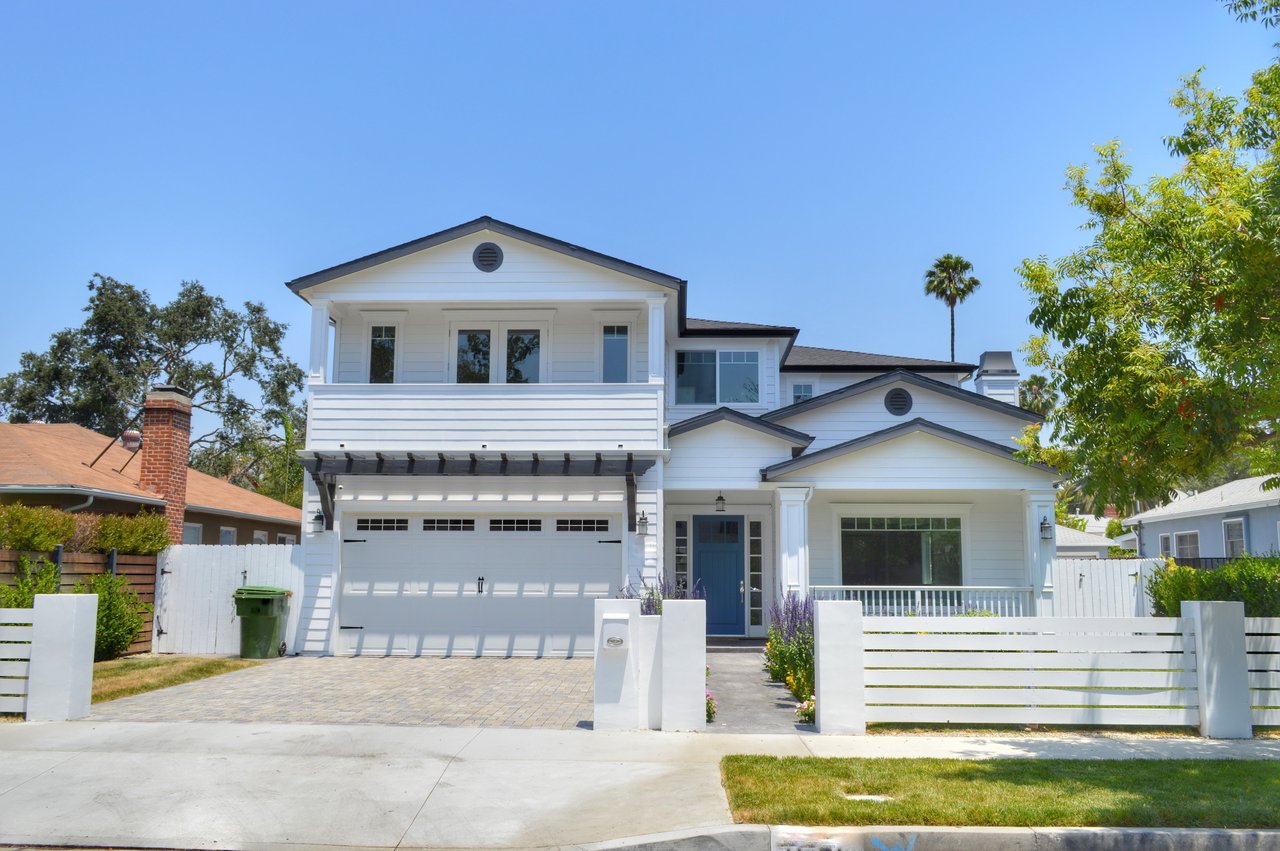 Two-story white house with a blue front door, wide garage, and white front fence.