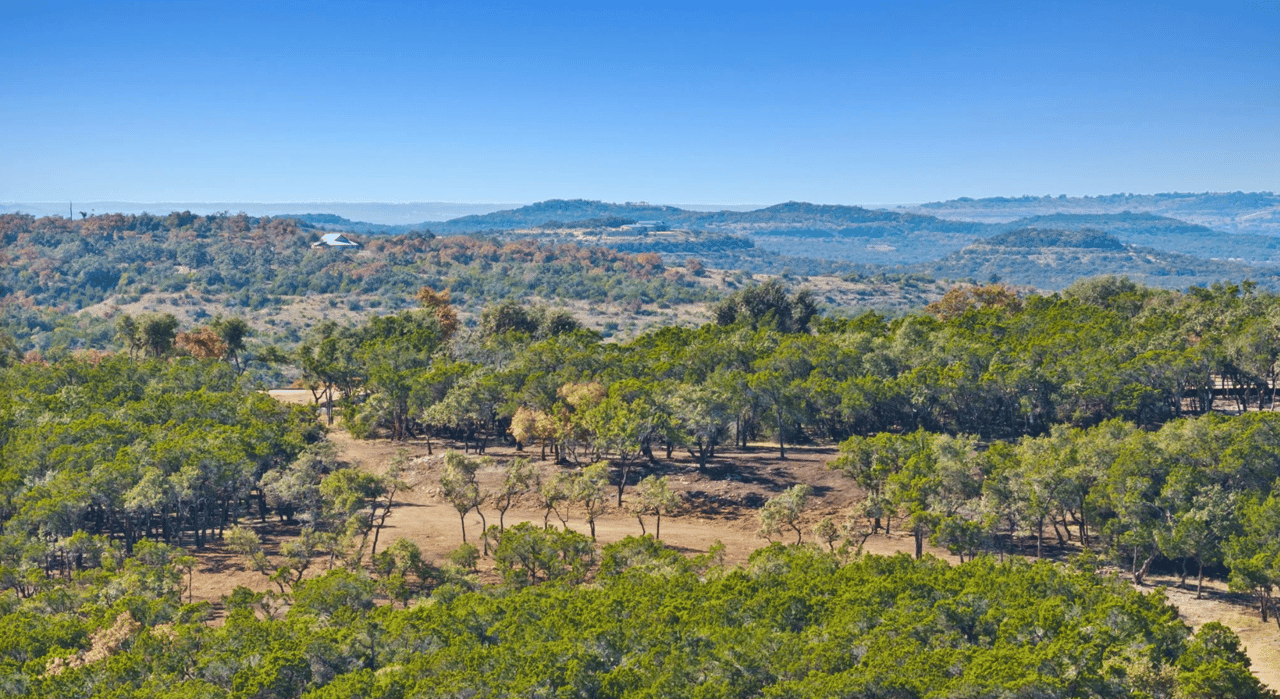 Aerial view of wooded ranch land with open clearings and rolling hills.