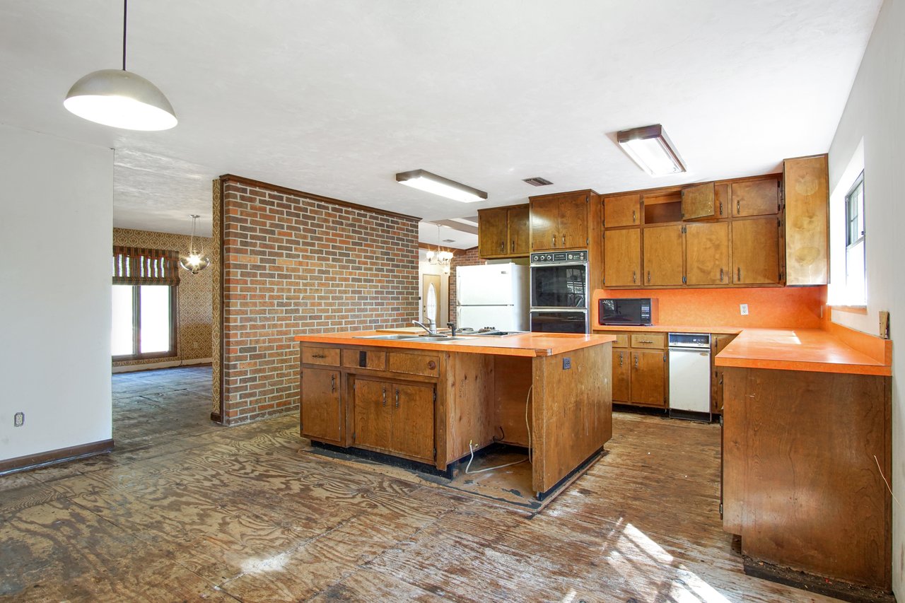 Vintage kitchen with a retro feel, featuring orange counters, dark wooden cabinets, and brick accent wall. Exposed flooring and ample natural light.