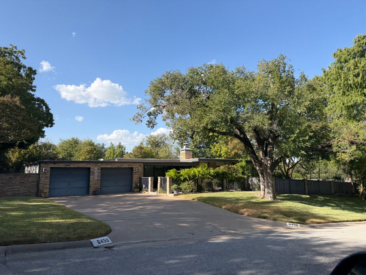 Single-story brick-and-stone home with two blue garage doors, a broad driveway, and a large shade tree.