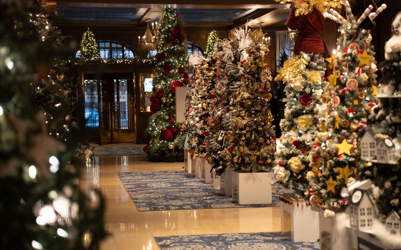 Decorated Christmas trees line an elegant lobby, covered in lights, ornaments, and gold accents.