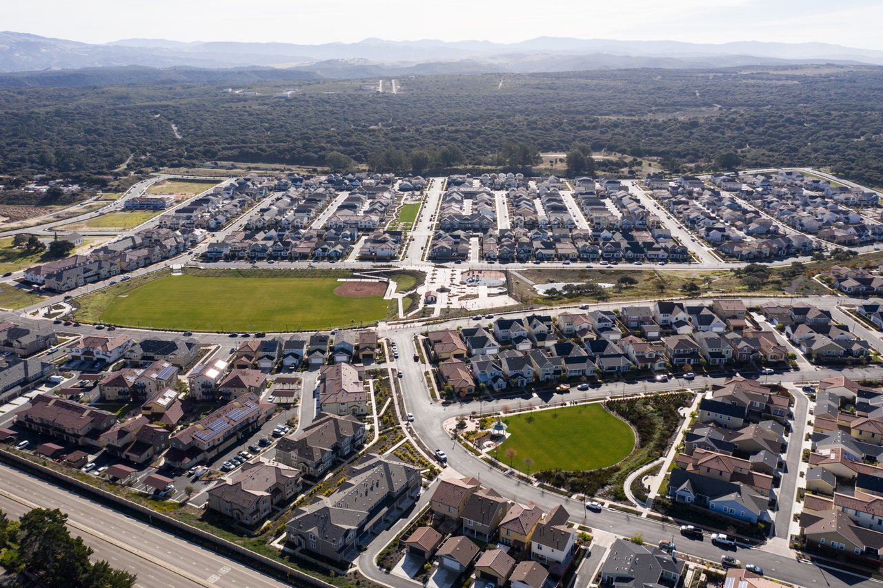 Aerial view of a residential community with rows of homes, green parks, and hills in the distance.