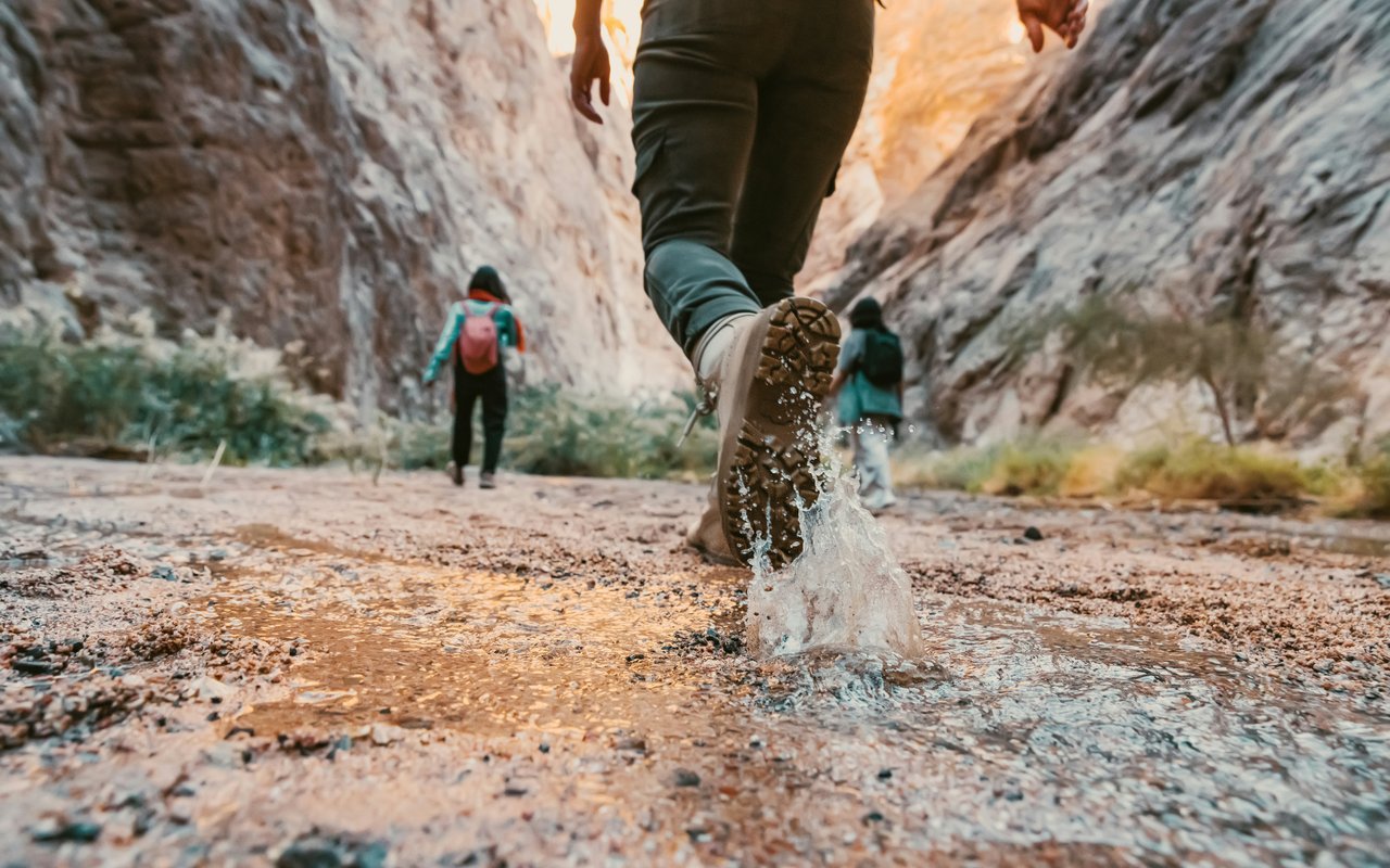Hikers wade through a shallow stream in a rocky canyon.
