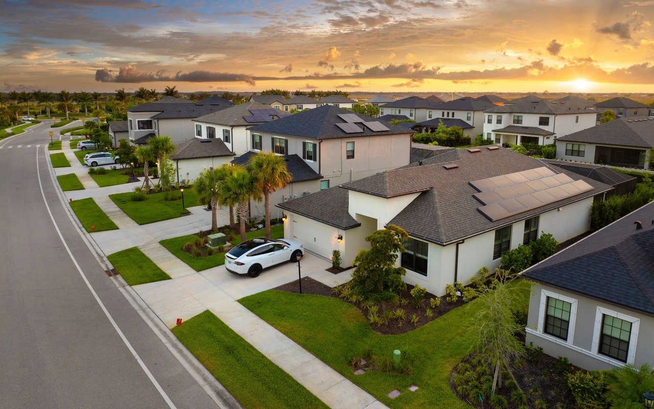 Aerial view of Trails homes with palm trees, landscaped lawns, and rooftop solar panels at sunset.