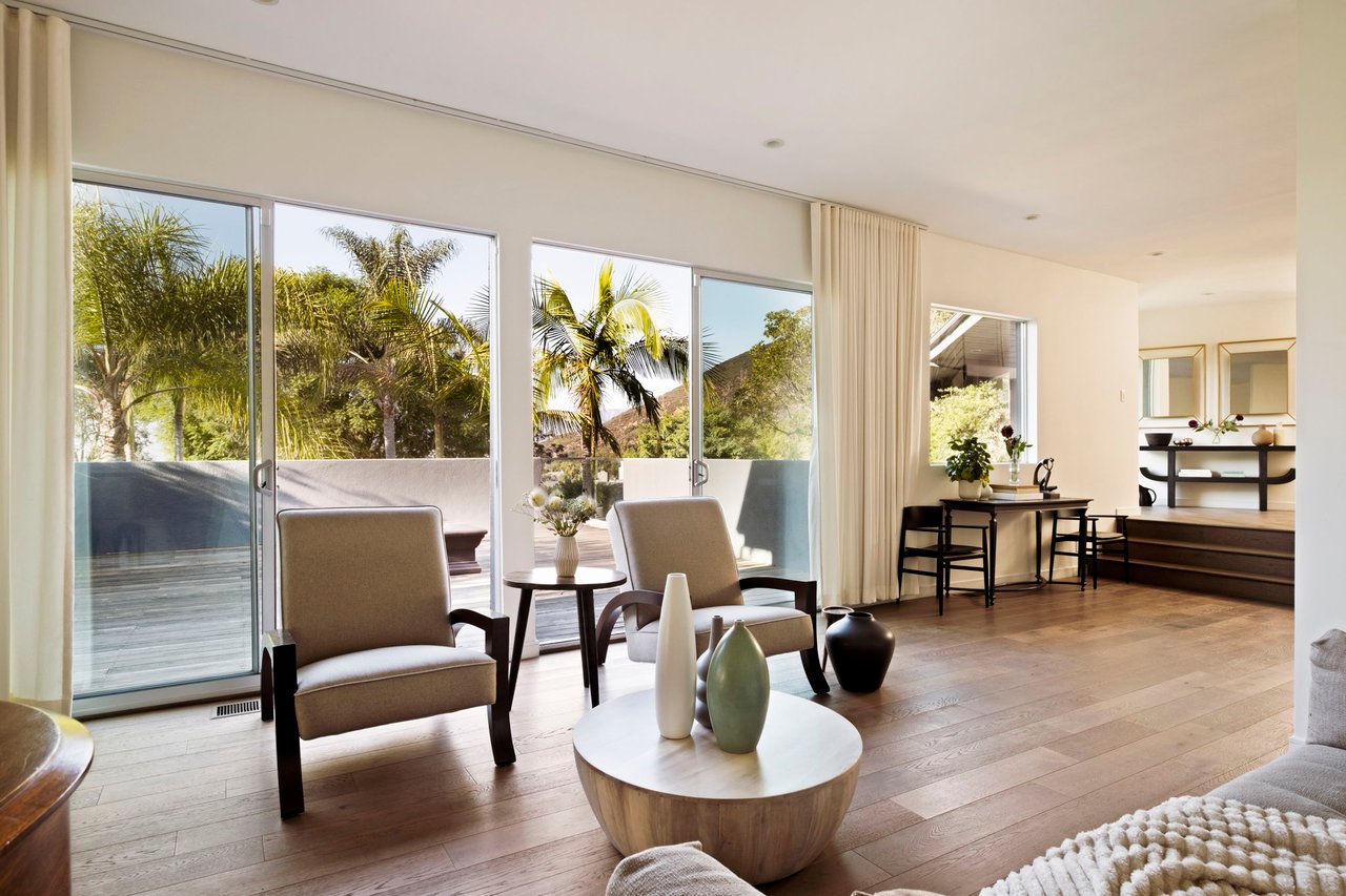 Furnished living room with wide sliding glass doors opening onto a palm-lined deck.