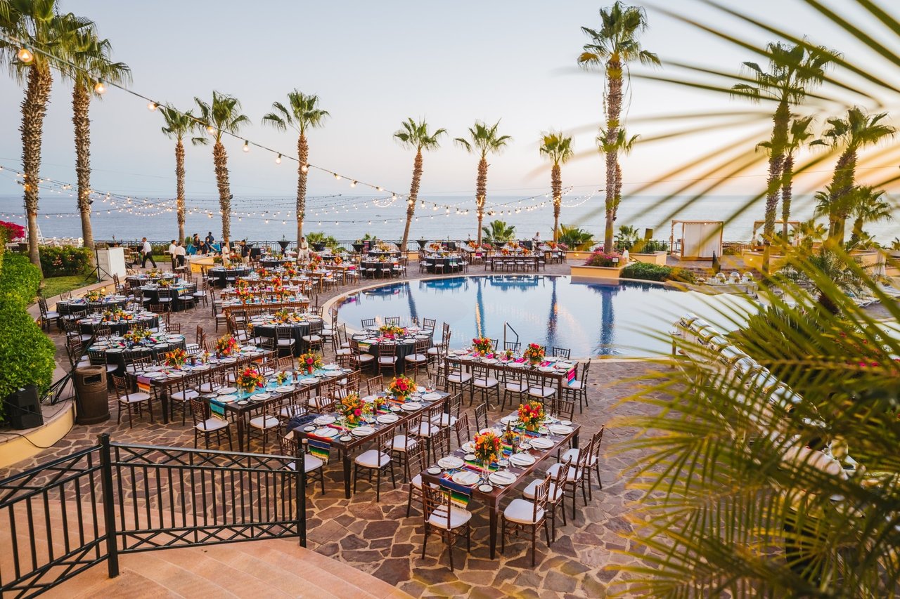 Pool terrace set with celebration tables and flowers, overlooking the ocean beneath string lights.