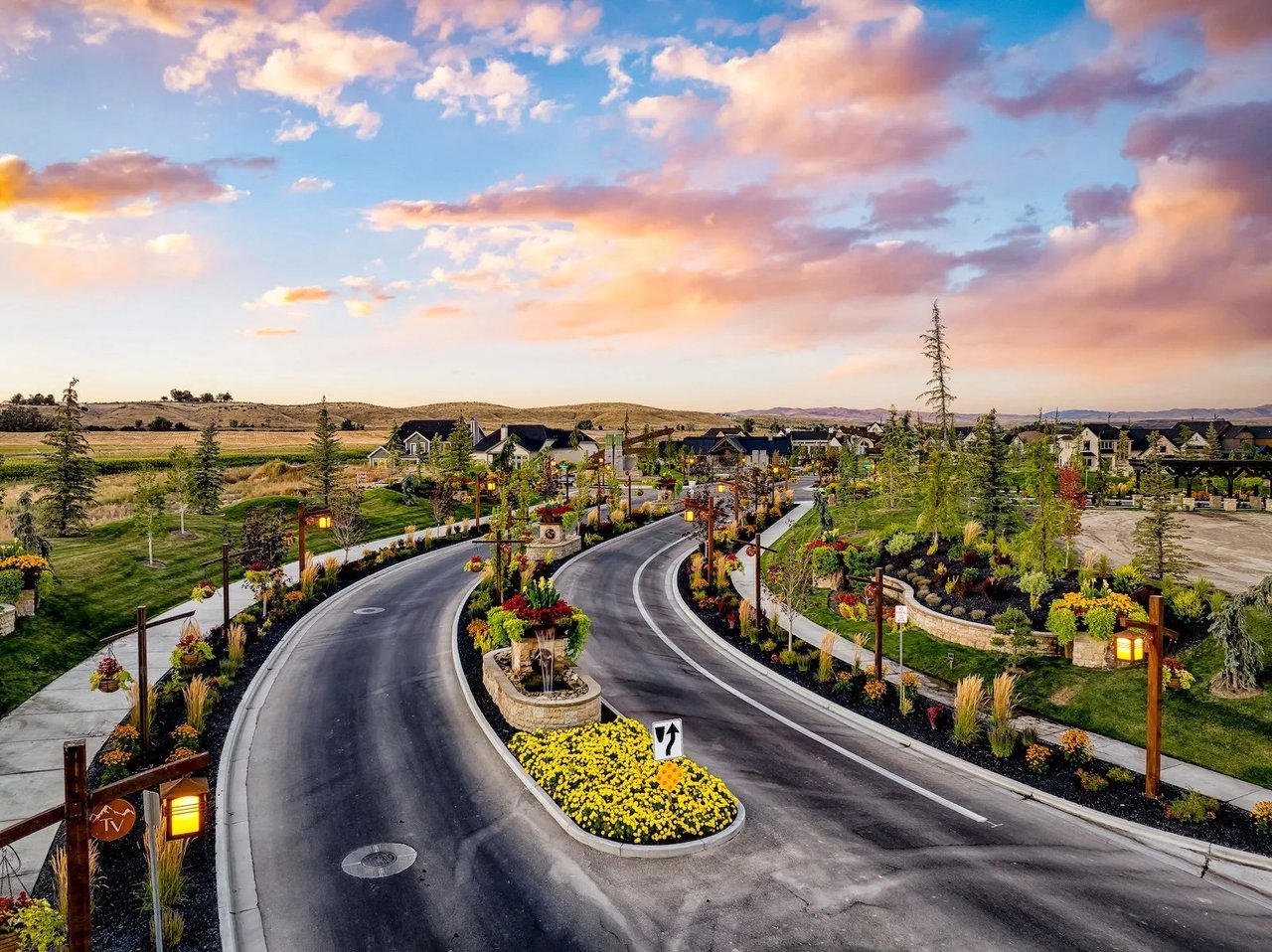 Landscaped Terra View neighborhood entrance with a curving road, flower-filled medians, and homes at sunset.