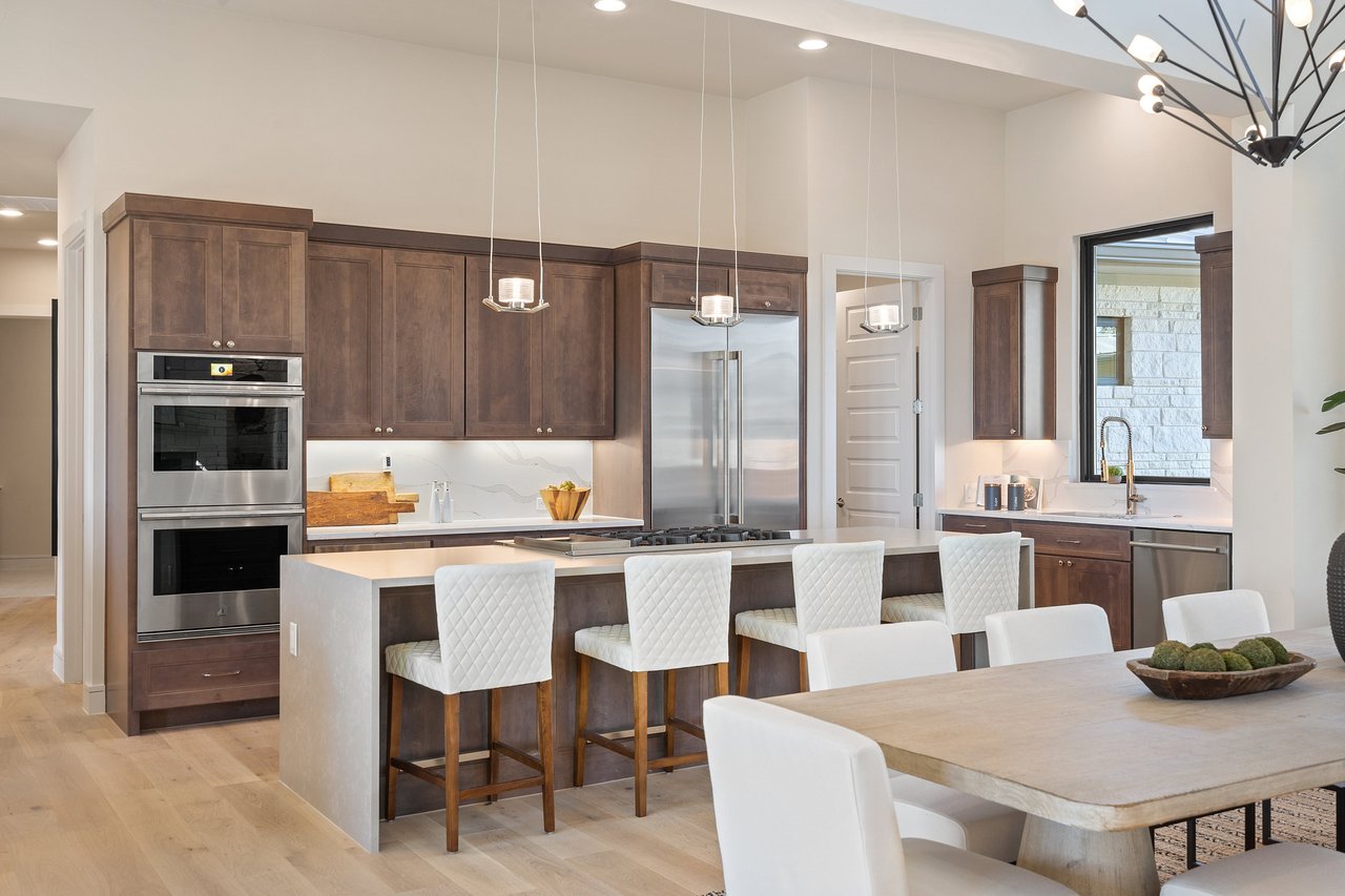 Chef's kitchen with an island, bar seating, stainless steel appliances, and wood cabinetry at this Bee Caves home on Caudill Lane, Austin, Texas.