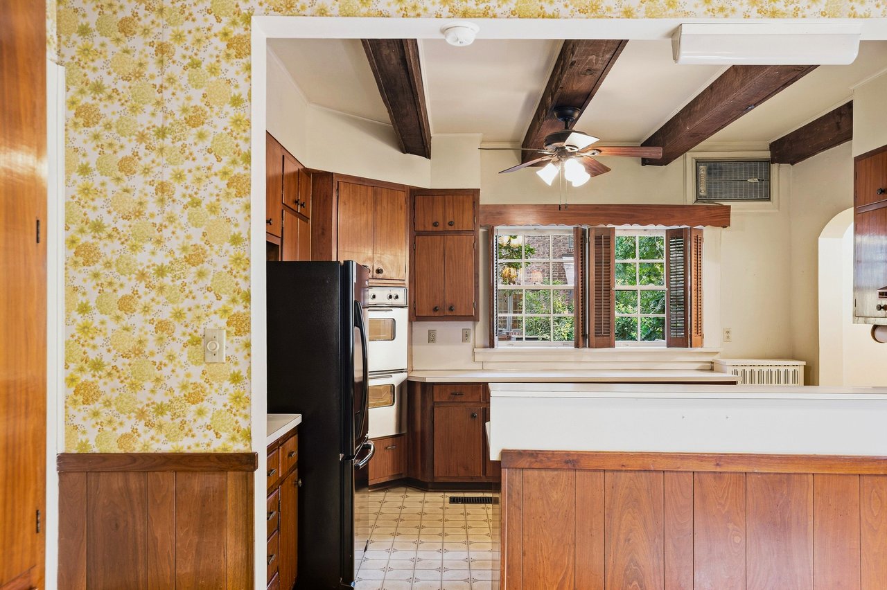 Kitchen with floral wallpaper, dark exposed ceiling beams, and a shuttered window.