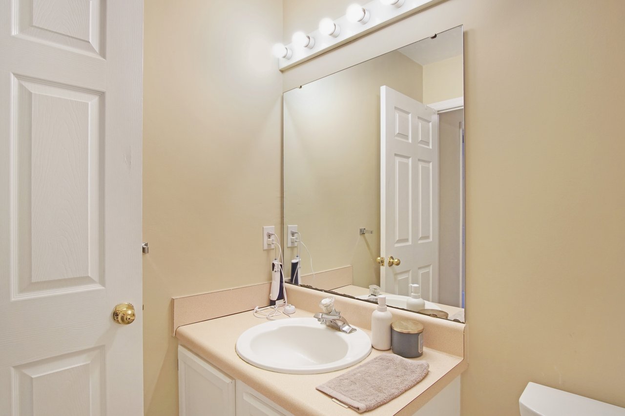 Bathroom at 529 Collinsford Road, Tallahassee, Florida, featuring a single-sink vanity with beige countertop, large wall mirror, and overhead lighting. The space includes white cabinetry, beige walls, and neatly arranged toiletries for a clean and simple design.