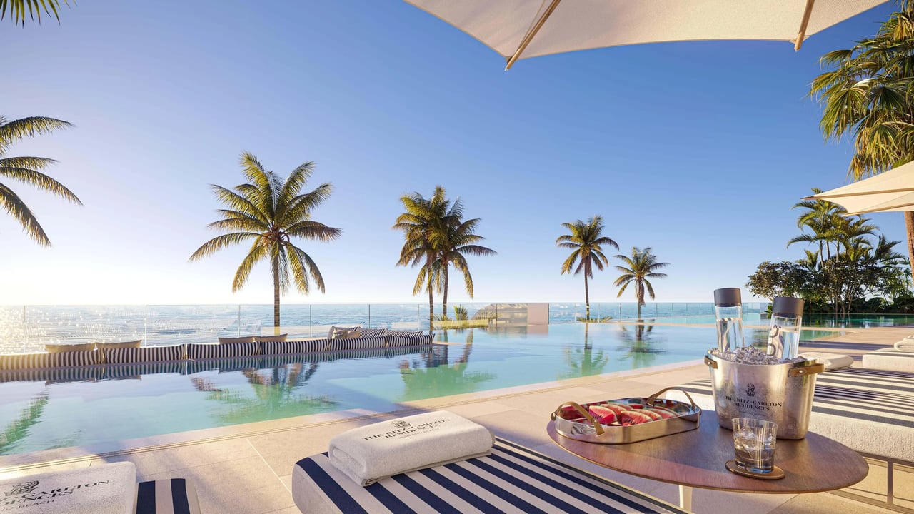 Oceanfront infinity pool with palm trees, striped loungers, and refreshments on a table.
