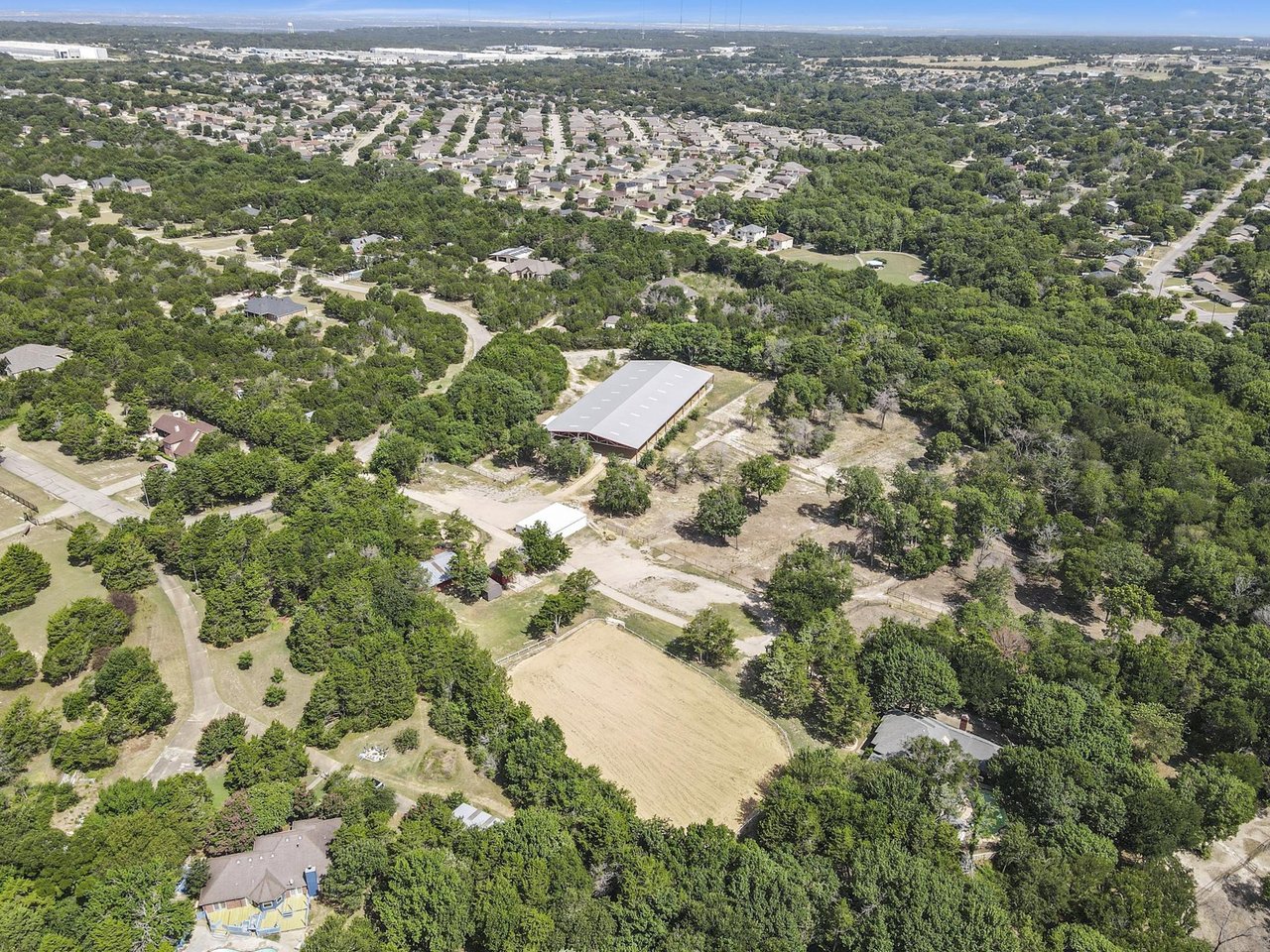 Aerial view of wooded land with a large metal-roofed building and a cleared area.